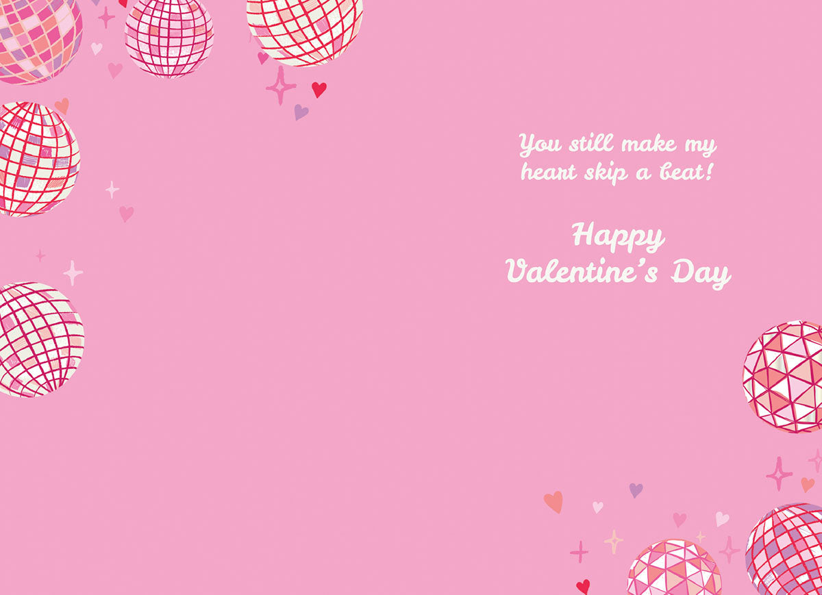 Inside of a pink greeting card with disco balls, hearts, and text 'You still make my heart skip a beat! Happy Valentine's Day'.
