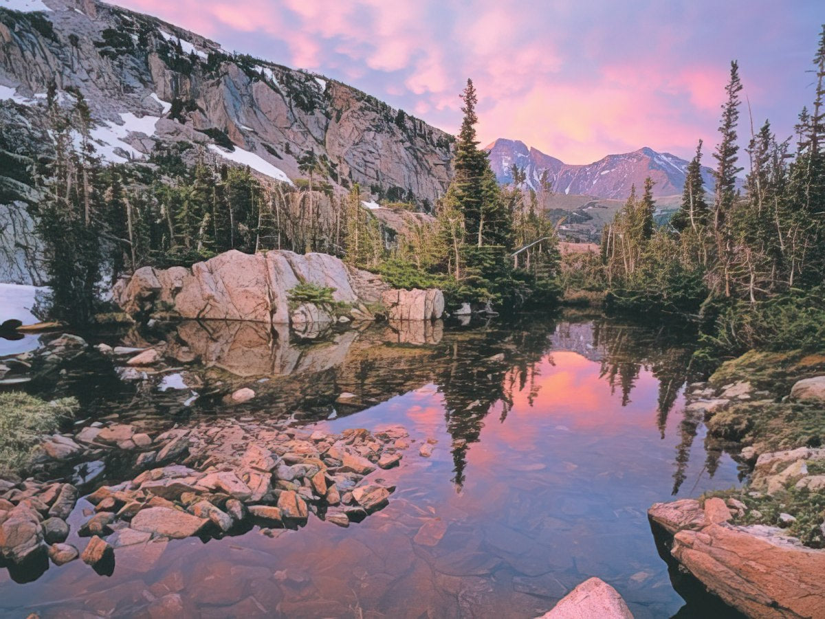 A serene mountain lake reflecting warm golden light on distant peaks and dark evergreen forests at sunset, John Fielder photo.
