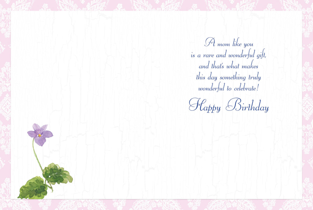 Open heartfelt greeting card revealing a warm message 'A mom like you is a rare and wonderful gift... Happy Birthday' on a soft pink background with a delicate purple flower illustration.