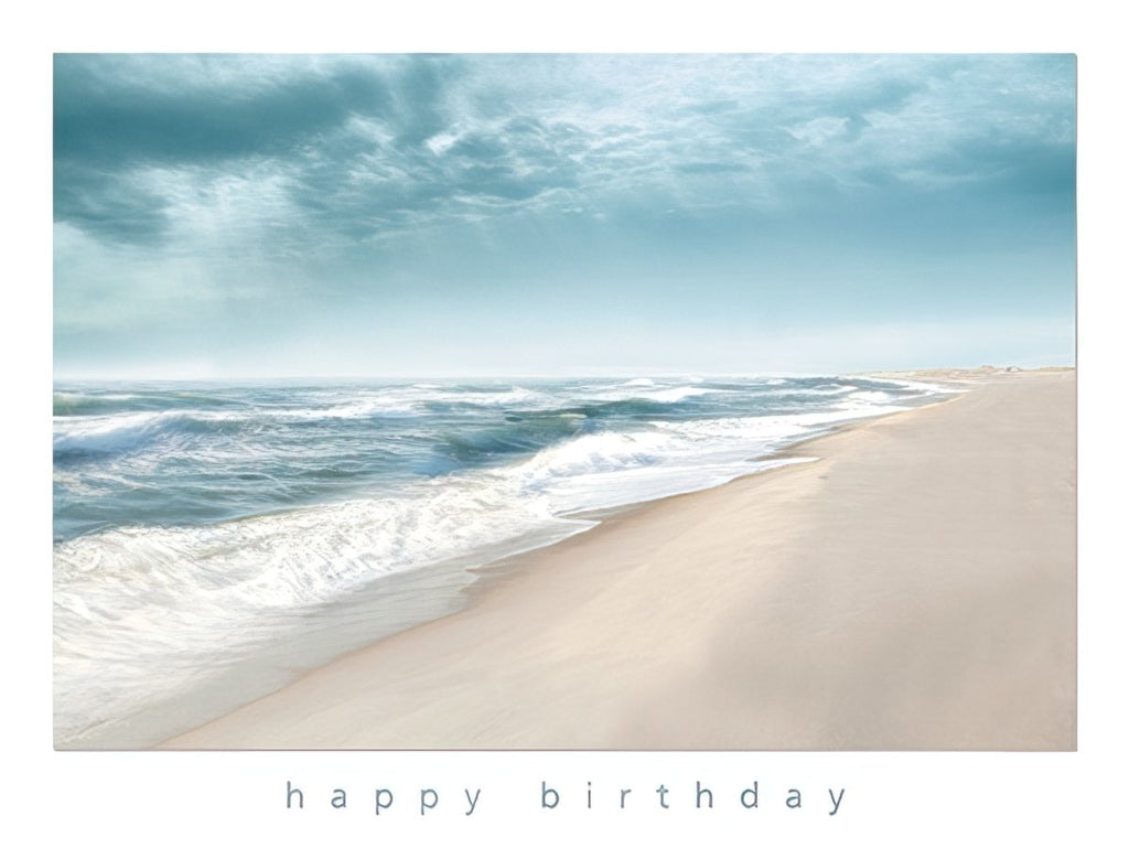 Front of a tranquil beach greeting card featuring gentle ocean waves, soft sandy shore, and a serene blue sky, with 'happy birthday' printed below.