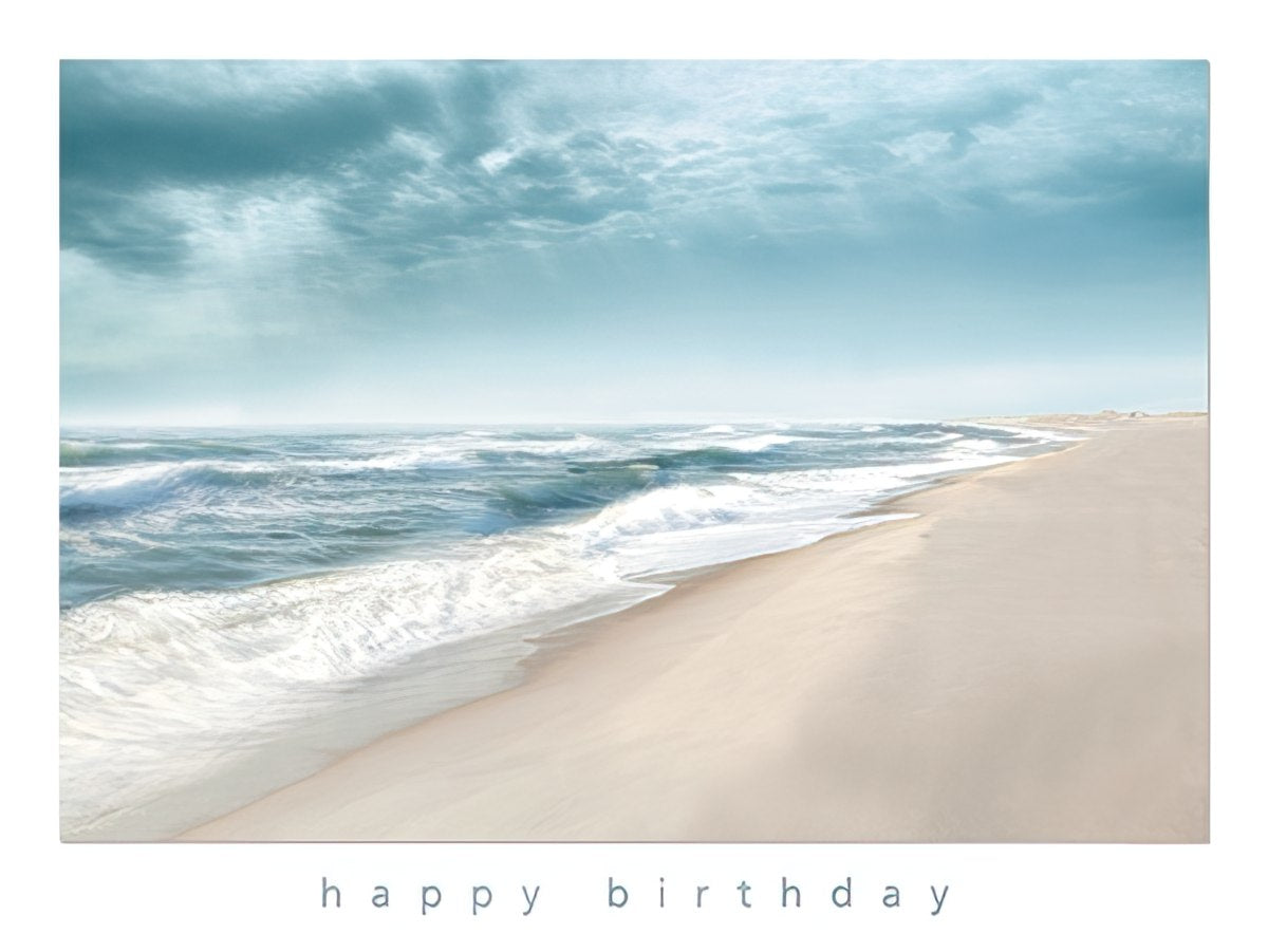 Front of a tranquil beach greeting card featuring gentle ocean waves, soft sandy shore, and a serene blue sky, with 'happy birthday' printed below.