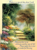 Front of a religious greeting card showing a colorful garden path with lush trees and blooming flowers. The text reads 'Today is a special day, dear Lord. Someone dear to me celebrates another year of life! Please make this a year of wonderful blessing.'