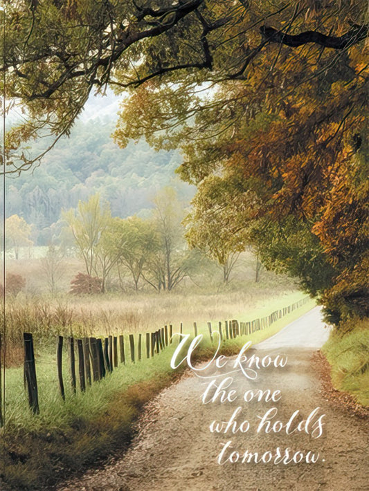 Greeting card featuring a scenic autumn road bordered by trees and a rustic fence, with the spiritual text 'We know the one who holds tomorrow.'
