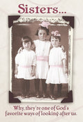 Vintage photo style magnet featuring three young sisters in white dresses with pink sashes and bows, embracing each other. Text reads 'Sisters... Why, they're one of God's favorite ways of looking after us.' promoting family bond and faith.