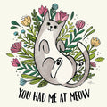 Whimsical grey and white cartoon cat magnet with black paws, lounging amidst vibrant pink, yellow, and blue flowers and green leaves. Features the playful text 'YOU HAD ME AT MEOW' in bold black font, perfect for cat lovers.