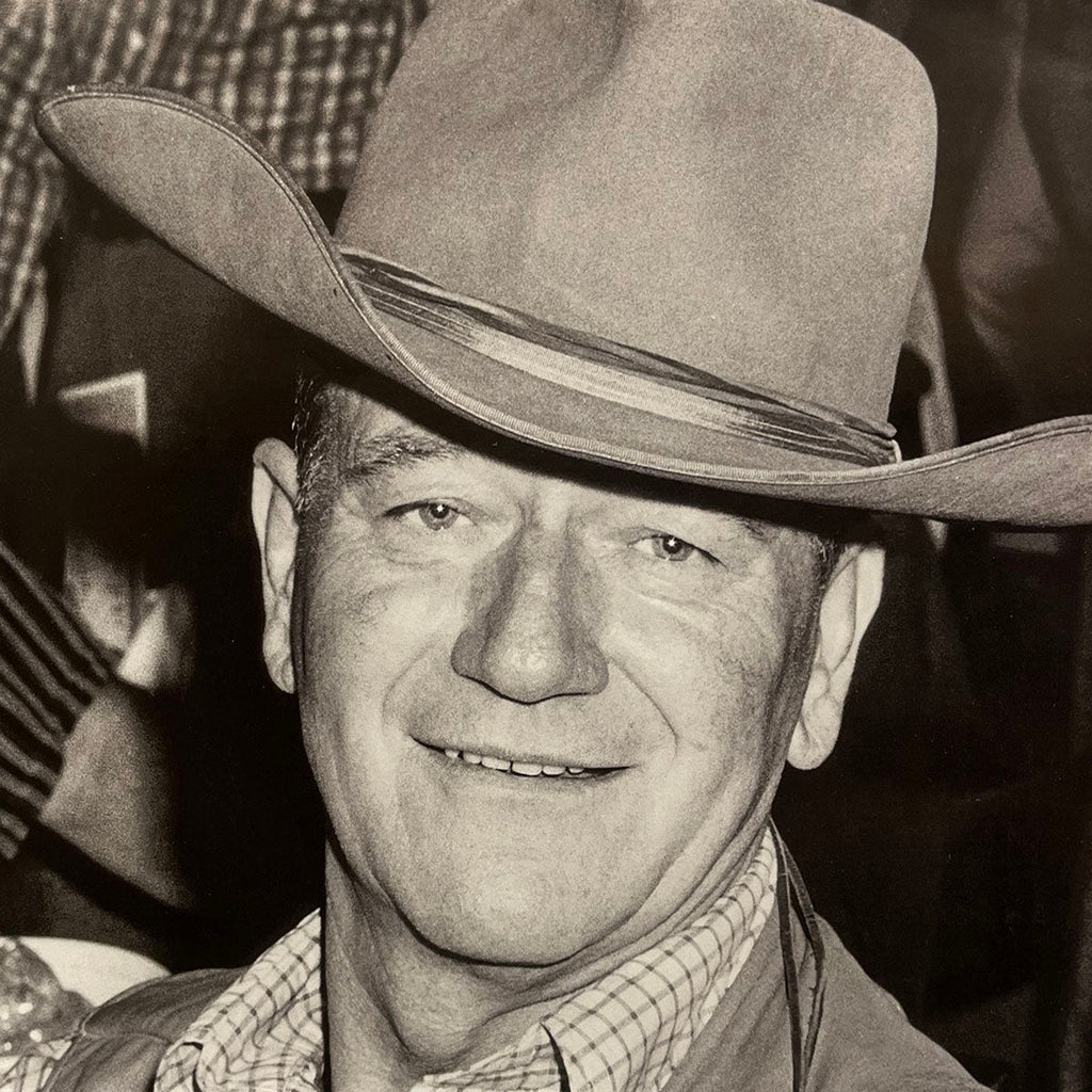 Classic black and white portrait of John Wayne smiling, wearing a cowboy hat, for the 2027 wall calendar.