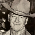 Classic black and white portrait of John Wayne smiling, wearing a cowboy hat, for the 2027 wall calendar.