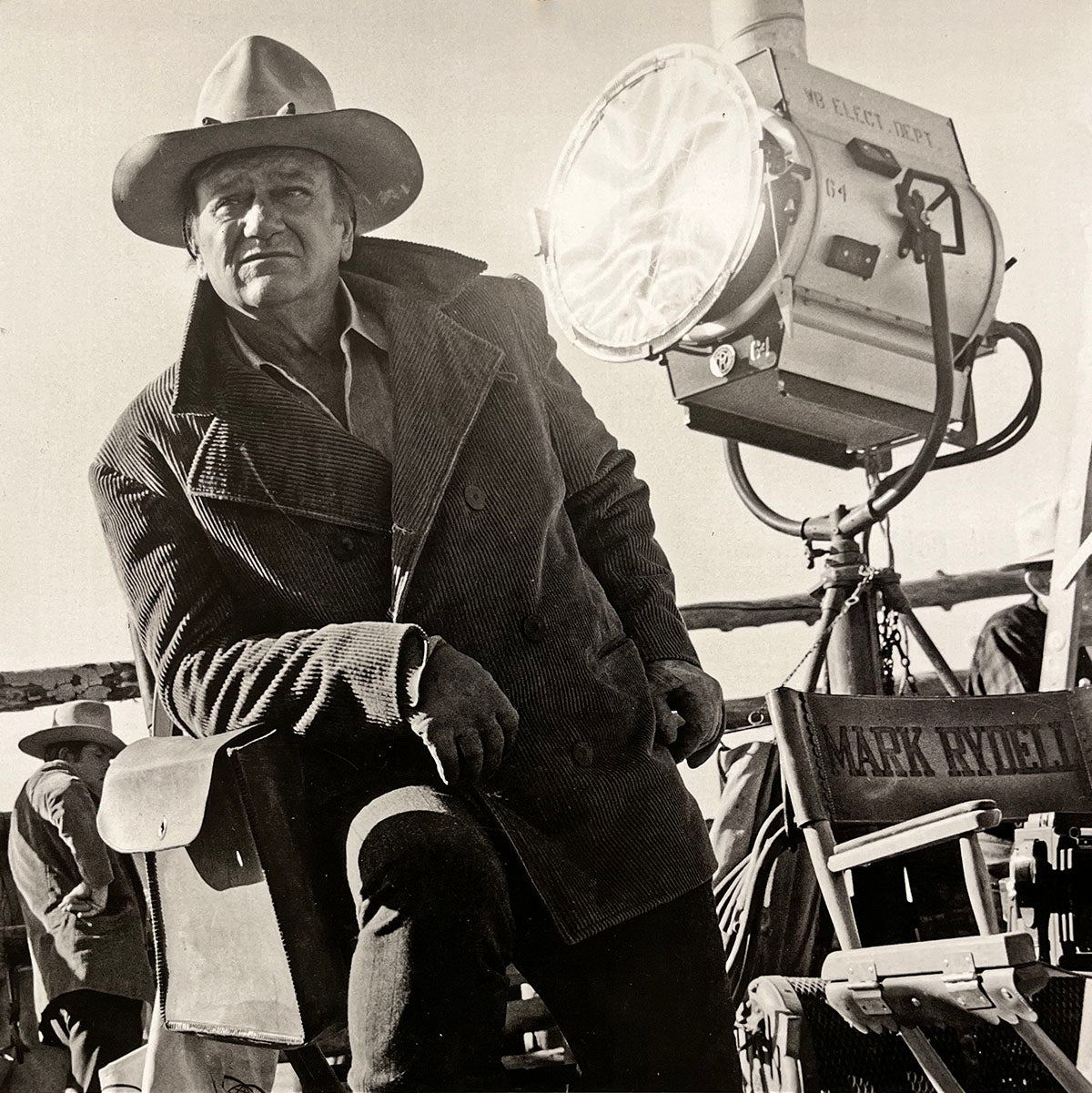 John Wayne in a robust coat and cowboy hat on a film set, leaning, from the collector's calendar.