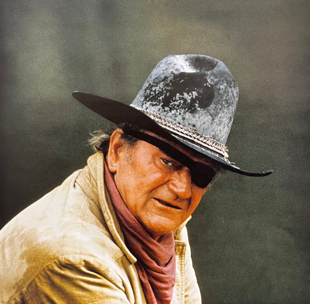 Intense close-up of John Wayne wearing an eye patch and a weathered cowboy hat, a memorable calendar image.