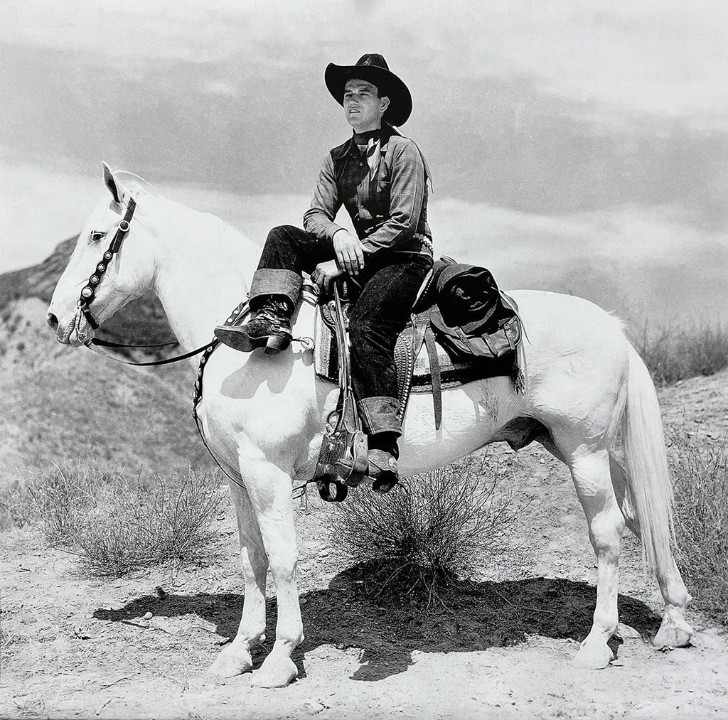 Young John Wayne looking confident, sitting atop a white horse in a vast western landscape, featured in the calendar.