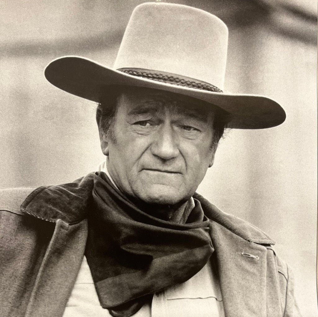 Close-up of John Wayne in a wide-brimmed cowboy hat and dark scarf, with a stern expression, for the annual calendar.