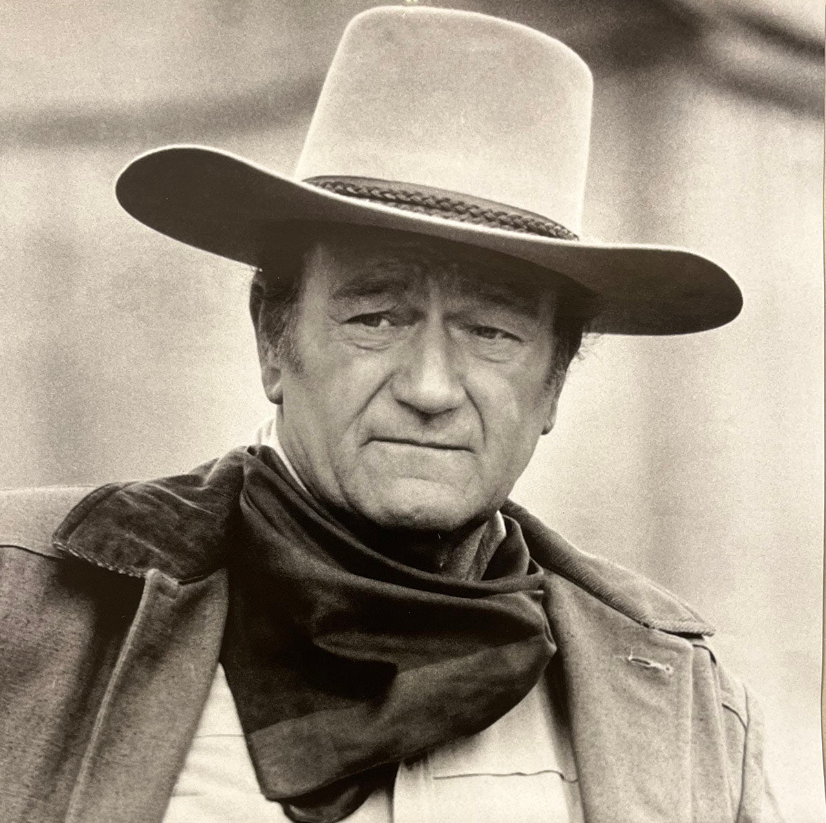 Close-up of John Wayne in a wide-brimmed cowboy hat and dark scarf, with a stern expression, for the annual calendar.