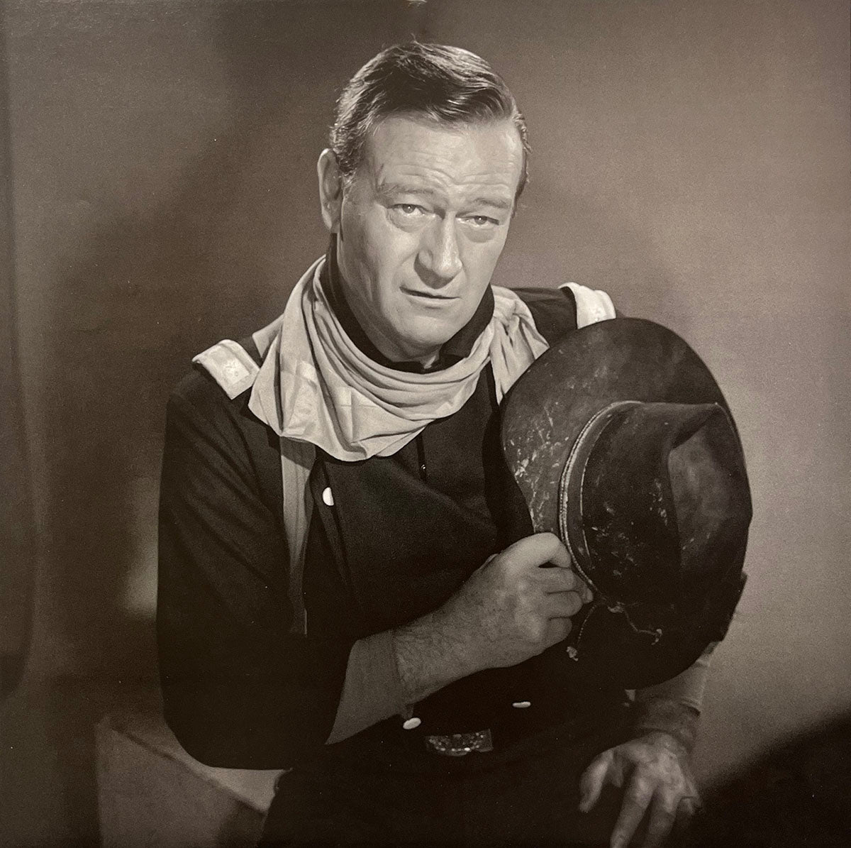 John Wayne in uniform, holding a cowboy hat, looking directly at the camera, a classic movie star calendar image.