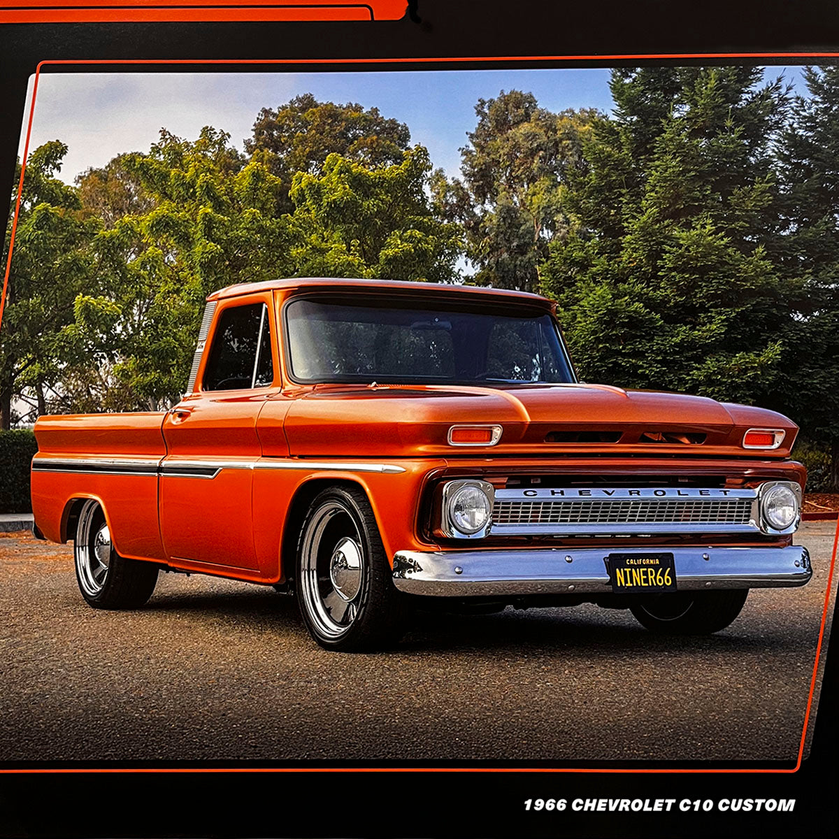 Side view of an orange 1966 Chevrolet C10 Custom pickup truck parked on asphalt with lush green trees in the background, showcasing its classic design and chrome accents.