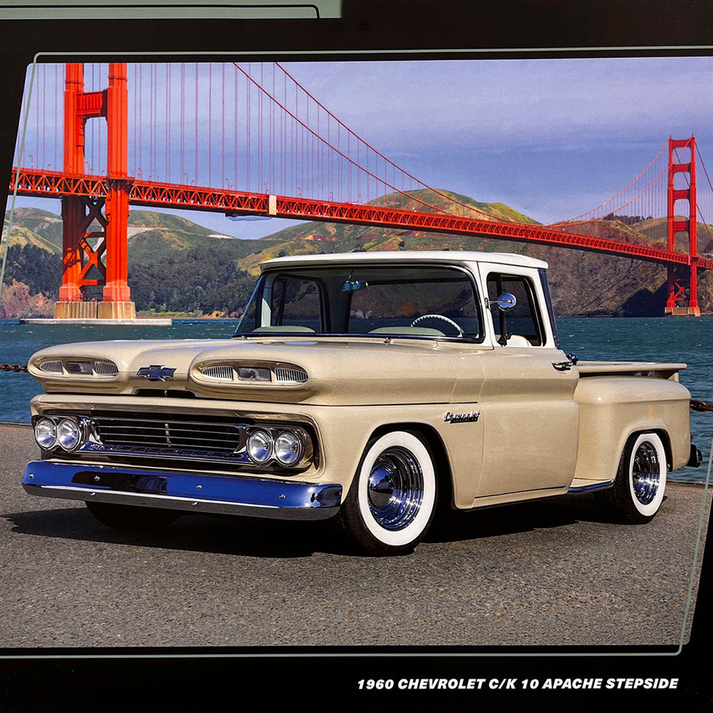 A beige 1960 Chevrolet C/K 10 Apache Stepside pickup truck with white wall tires, parked by the water with the iconic Golden Gate Bridge visible in the background under a blue sky.
