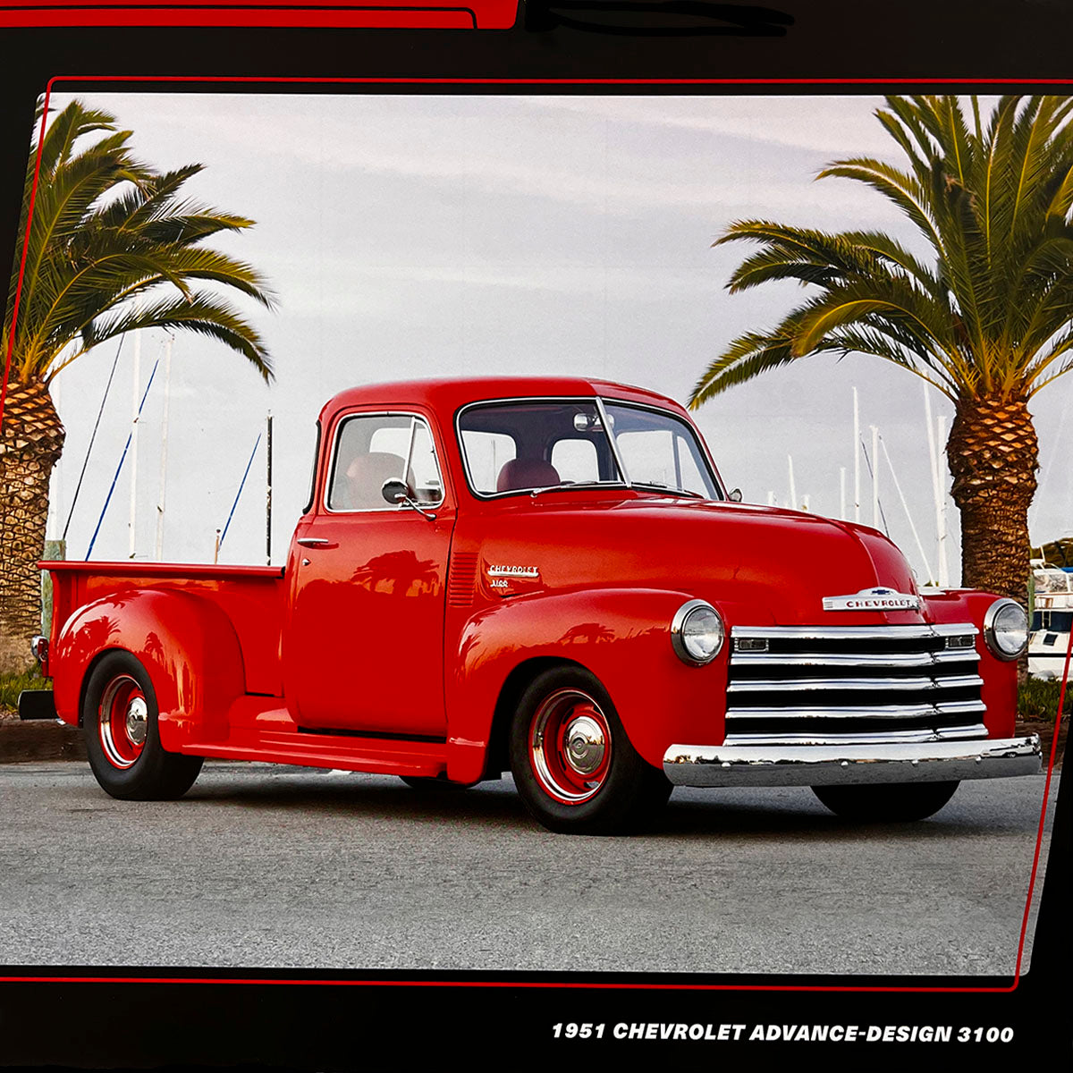 A bright red 1951 Chevrolet Advance-Design 3100 pickup truck with chrome grill and red wheels, parked in front of palm trees and a marina, exuding vintage charm.