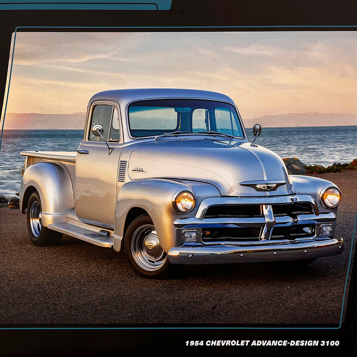 A sleek silver 1954 Chevrolet Advance-Design 3100 pickup truck parked by the ocean at sunset, its chrome accents reflecting the warm light and showcasing its timeless beauty.