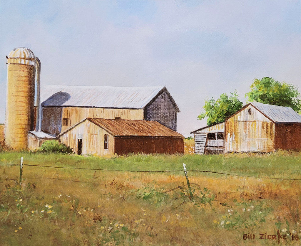 Rustic farm complex with multiple weathered barns and a silo in a golden summer field, captured by Bill Zierke.