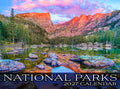 Stunning sunrise over Dream Lake in Rocky Mountain National Park, reflecting vibrant pink and purple skies, evergreen trees, and rugged peaks; cover image for a 2027 National Parks wall calendar.