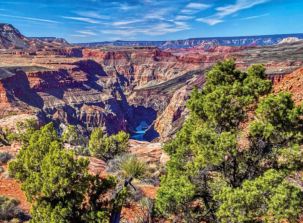 Grand Canyon aerial view with winding Colorado River, lush green trees, majestic red rock formations, and clear blue sky, ideal for a 2027 nature calendar.