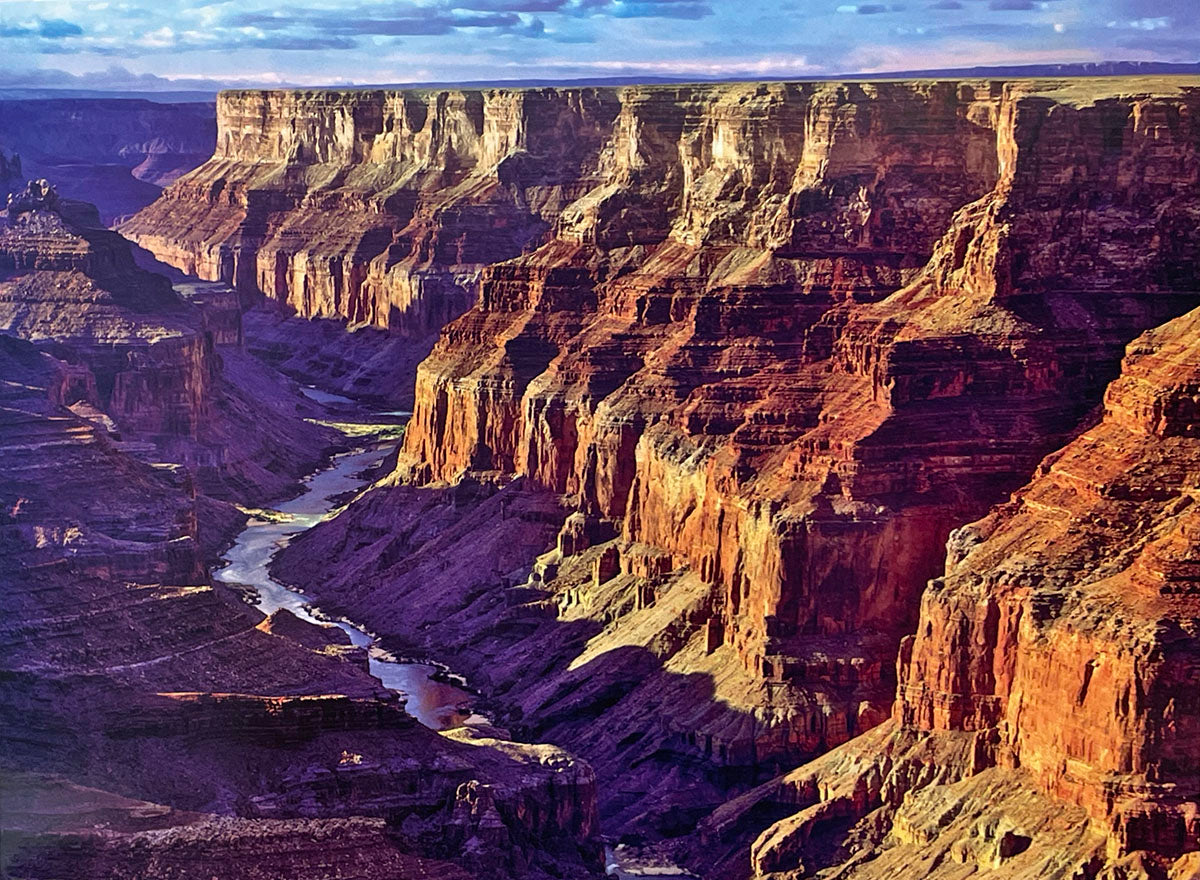 Panoramic view of the Grand Canyon's layered rock walls and a winding river far below, illuminated by the sun, emphasizing its geological formations for a scenic calendar.