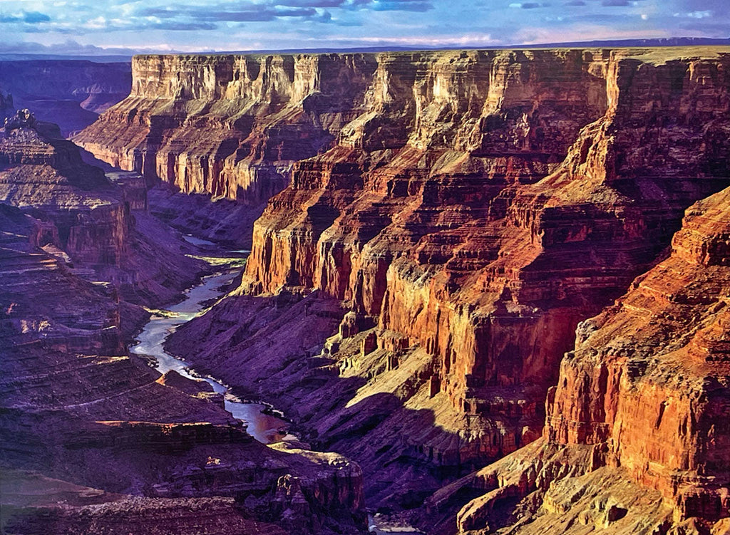 Panoramic view of the Grand Canyon's layered rock walls and a winding river far below, illuminated by the sun, emphasizing its geological formations for a scenic calendar.