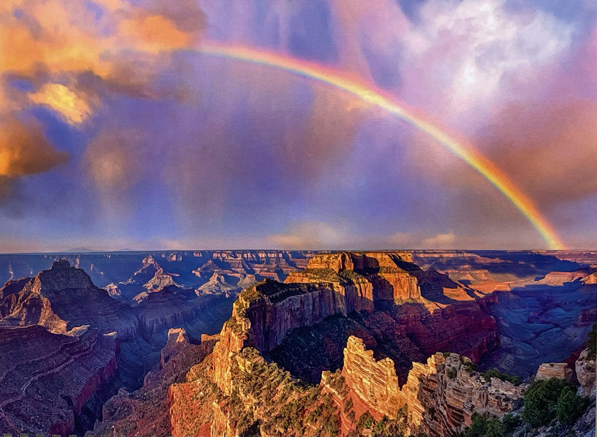 Expansive Grand Canyon vista under a vibrant sky with a prominent rainbow arching over the colorful rock formations, symbolizing hope and beauty in a nature calendar.