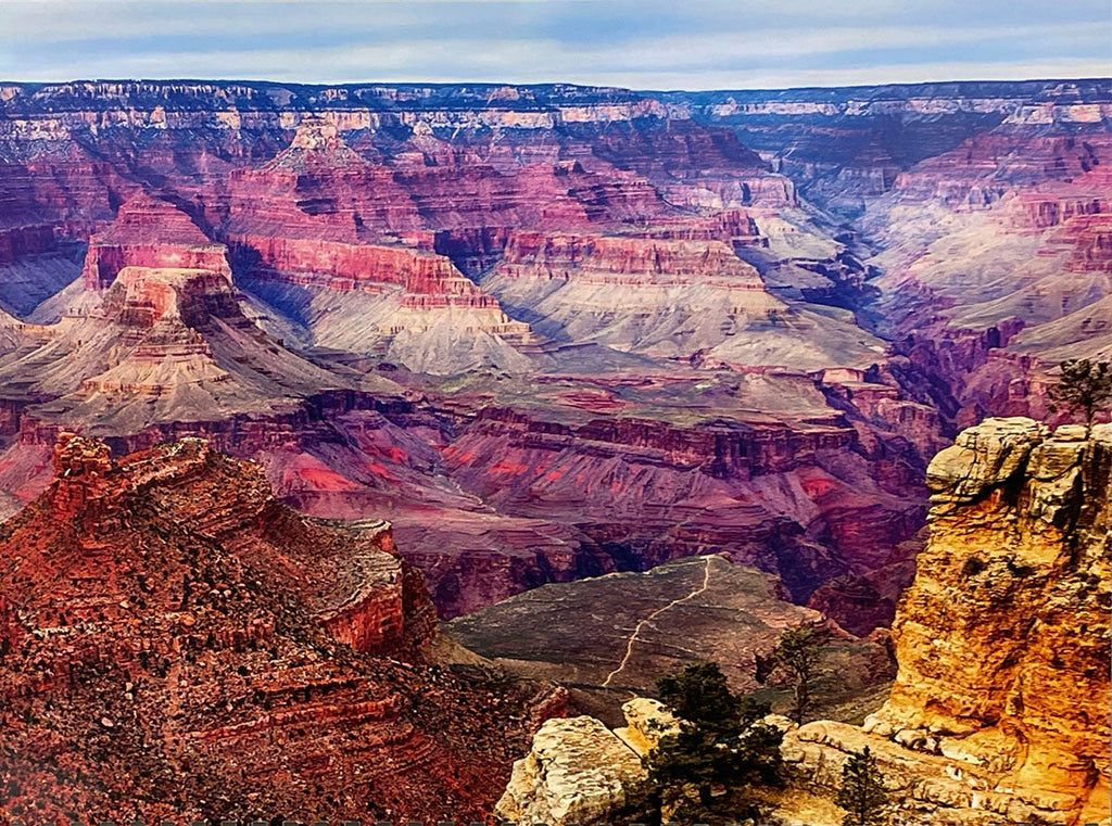 Wide shot of the Grand Canyon's South Rim, displaying intricate red, orange, and purple rock layers with a distant winding path and sparse vegetation, perfect for a Grand Canyon calendar.
