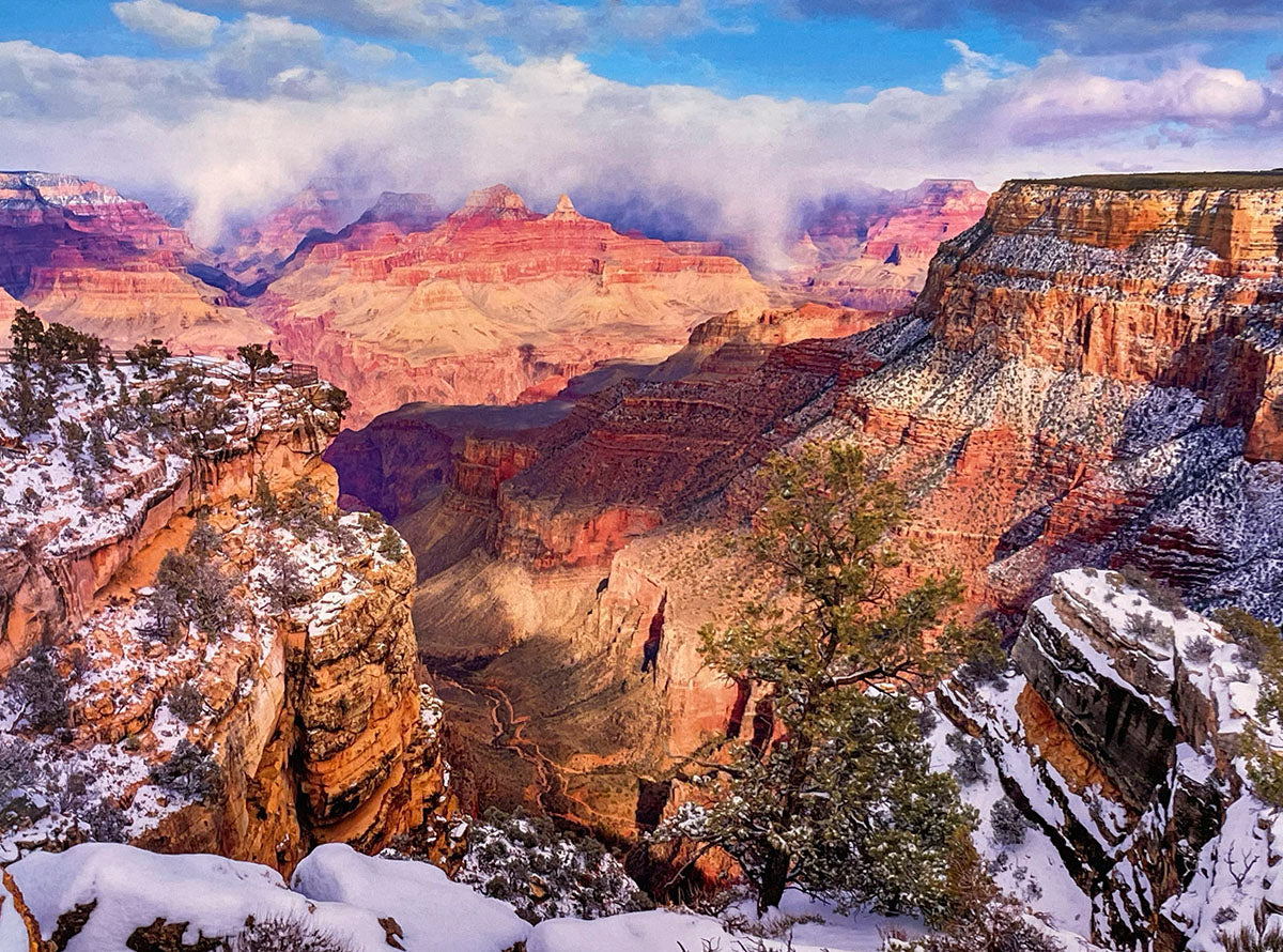 Winter scene at the Grand Canyon with snow-dusted red rock formations, pine trees, and a misty canyon floor under a cloudy sky, showcasing seasonal beauty for a monthly planner.
