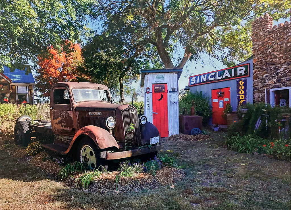 Rustic scene with a weathered vintage Dodge truck parked in front of an old Sinclair Goods store and outhouse.