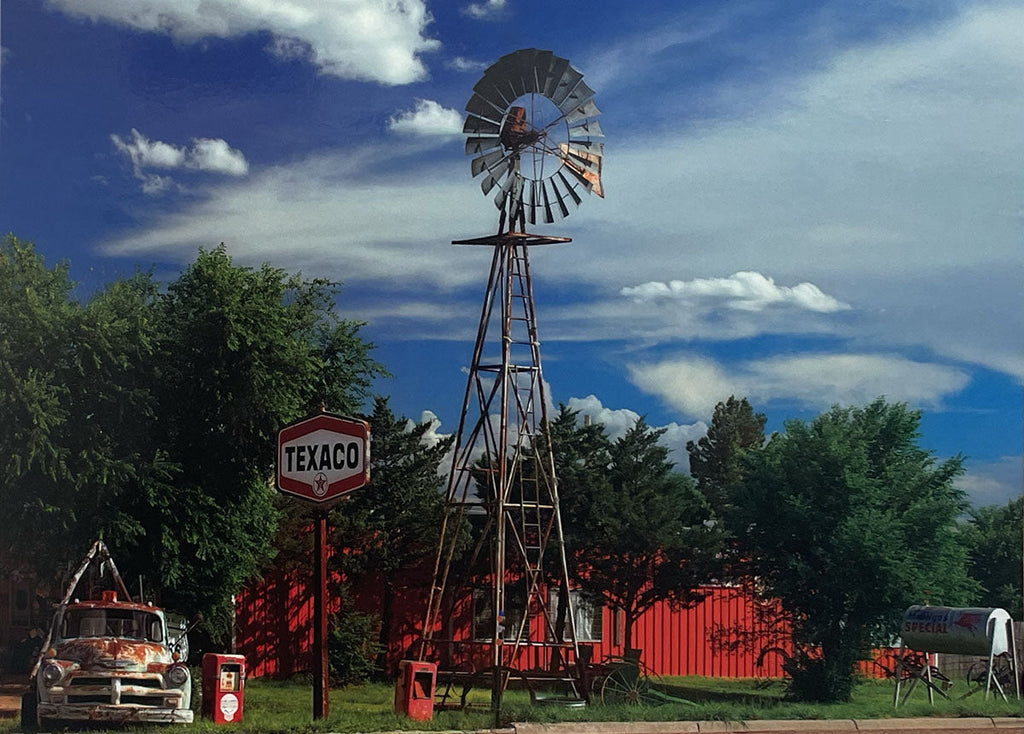 Old Texaco sign and a tall, rustic windmill standing in a green field under a blue sky, classic Americana.