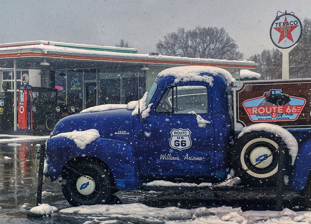 Charming blue vintage pickup truck adorned with Route 66 signage, covered in snow in Williams, Arizona.