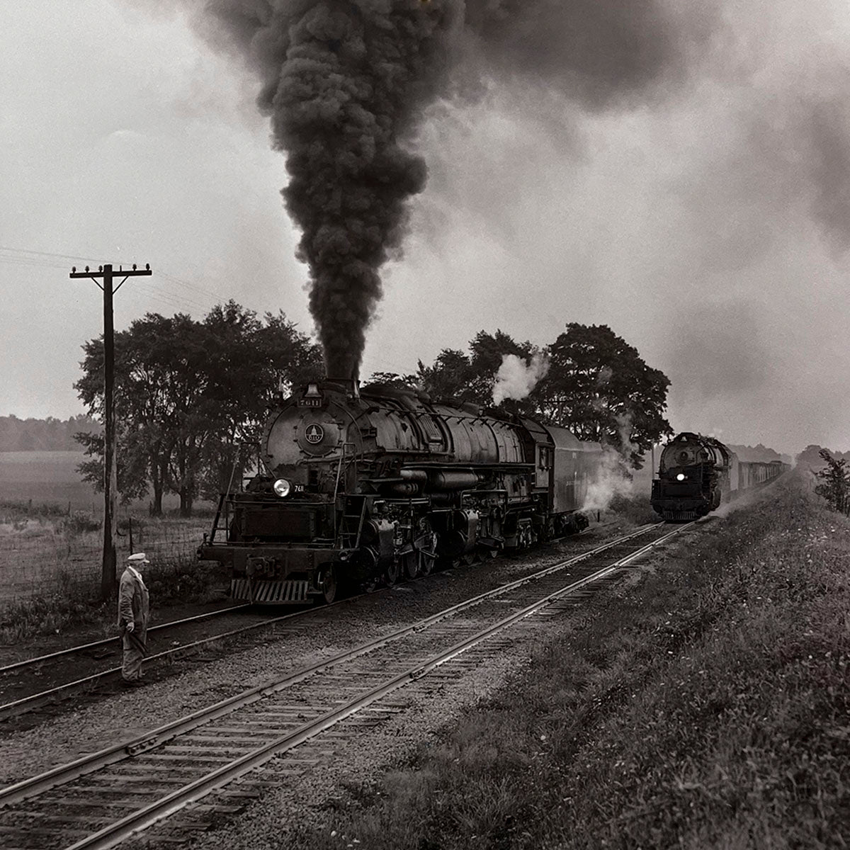 Two powerful steam locomotives on parallel tracks, one billowing smoke, with a railroad worker standing beside the tracks in a rural landscape, historic train meet, rail operations.