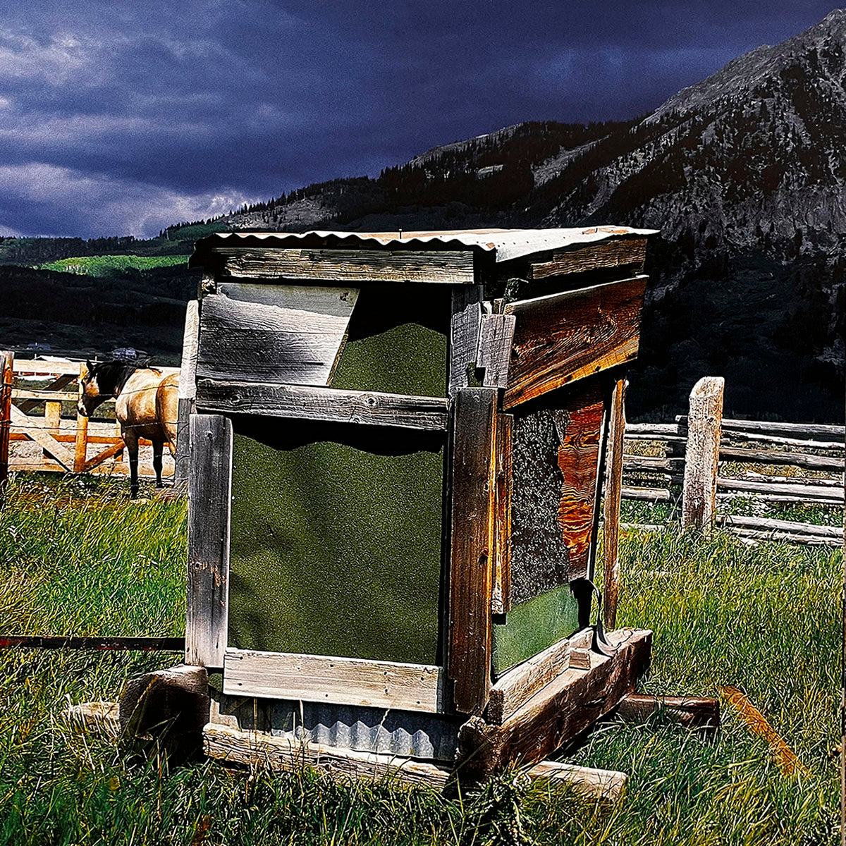 January 2027 calendar image: A unique, patched-up wooden outhouse with a green panel, set in a grassy field with a wooden fence and a horse in the distance, dramatic mountains under dark clouds.