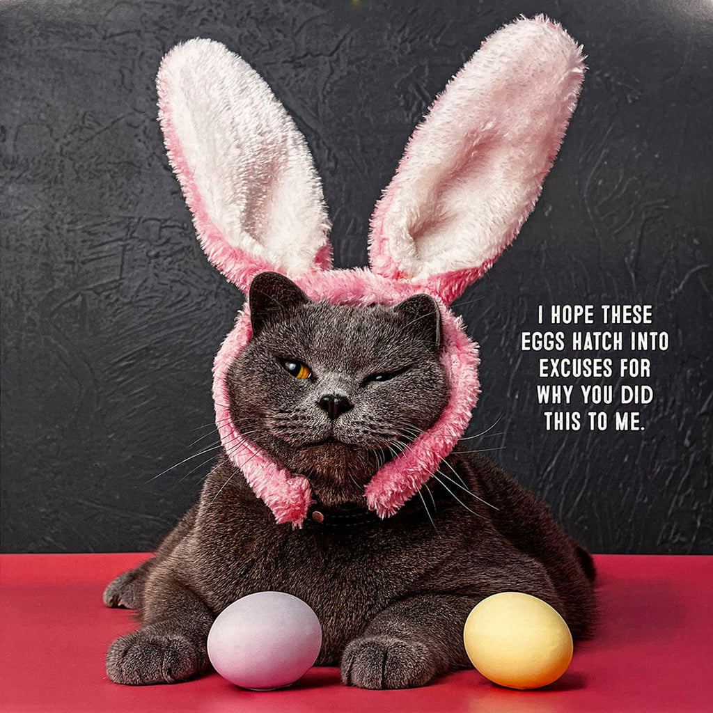 Sarcastic cat calendar photo depicting a grumpy grey cat wearing pink bunny ears, sitting between two Easter eggs. Caption: 'I hope these eggs hatch into excuses for why you did this to me.'
