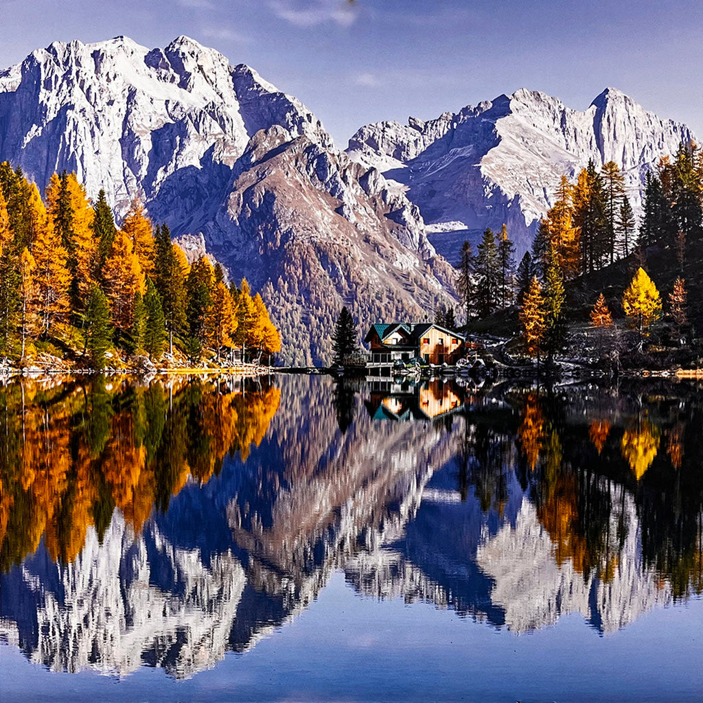 Picturesque mountain lake reflecting snow-dusted peaks and vibrant autumn trees surrounding a quaint lakeside cabin.
