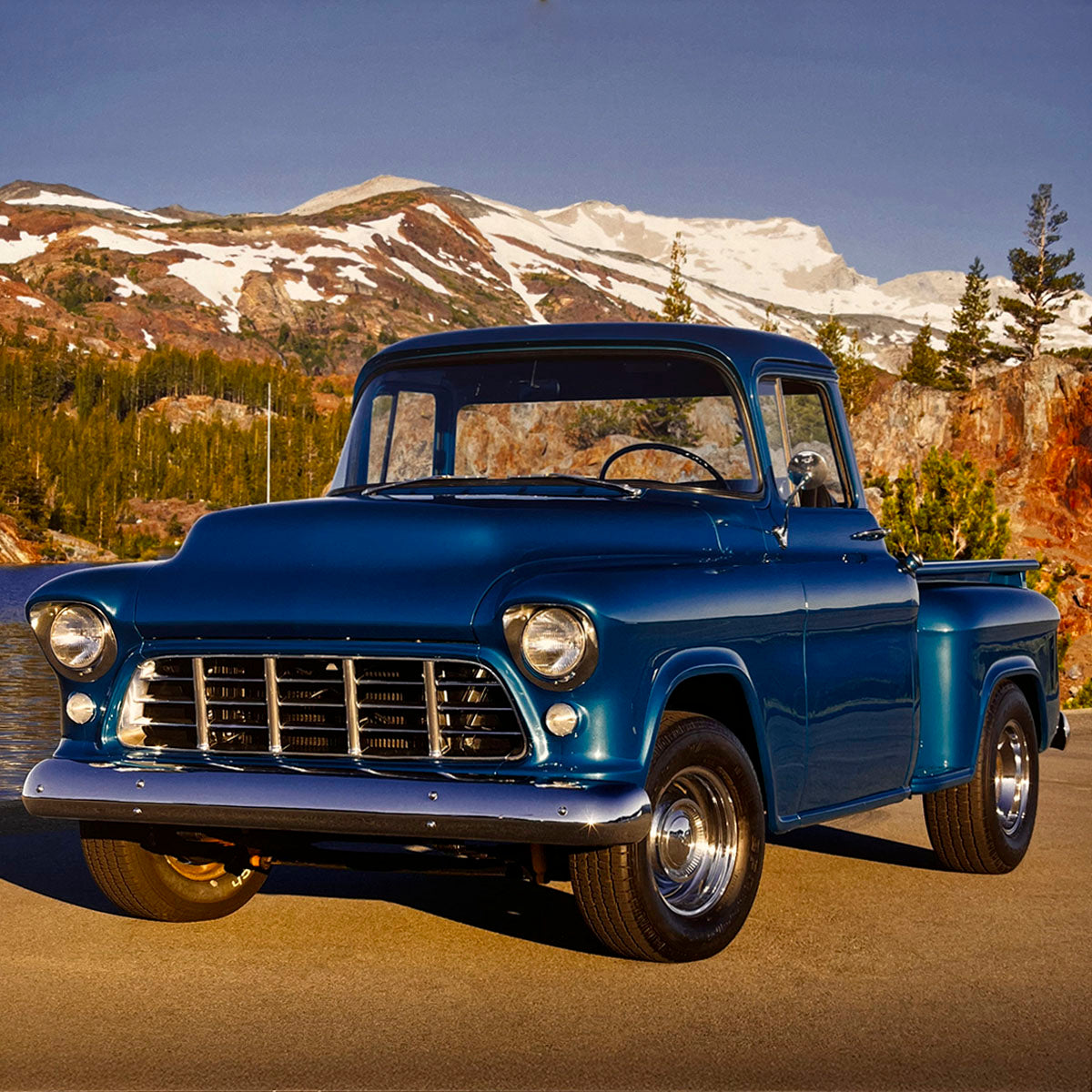 A stunning blue 1957 Chevrolet 3100 pickup truck, featuring a chrome grille and shiny wheels, set against a majestic backdrop of snow-capped mountains and a serene lake, perfect for vintage truck enthusiasts.