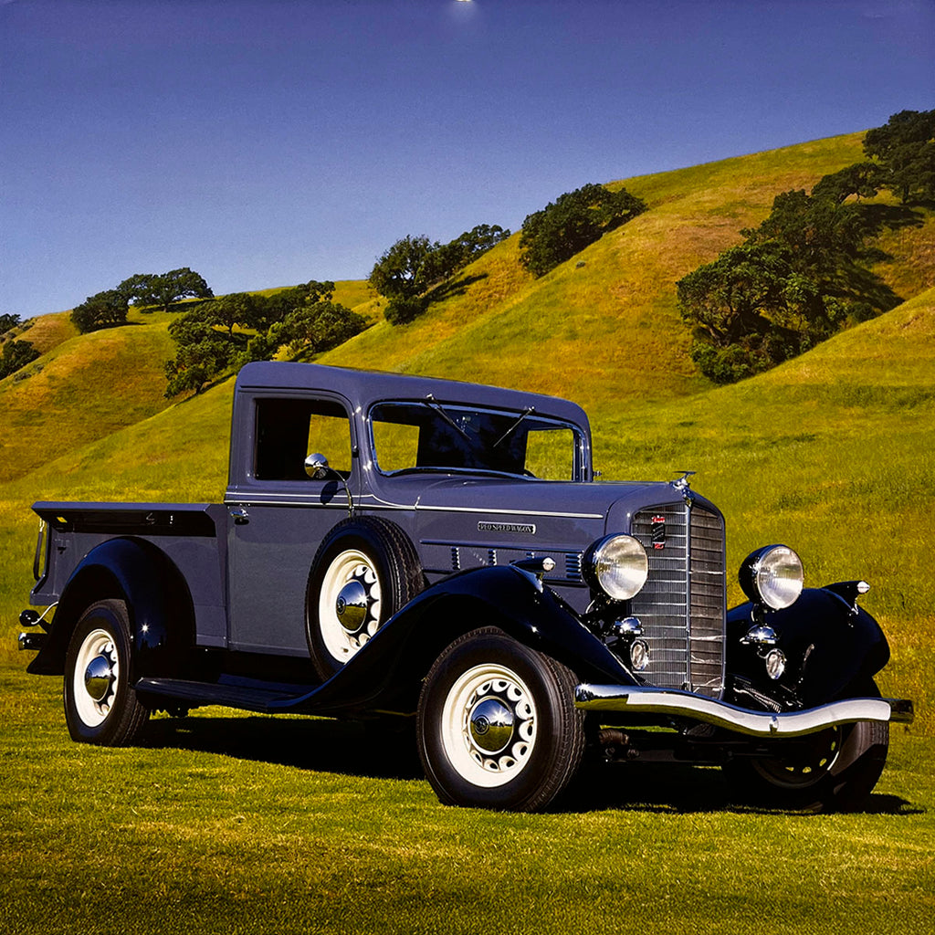 A stately dark grey 1937 International C-1 pickup truck with black fenders and white wall tires, resting on a verdant grassy hill against a bright blue sky, a testament to classic truck engineering.