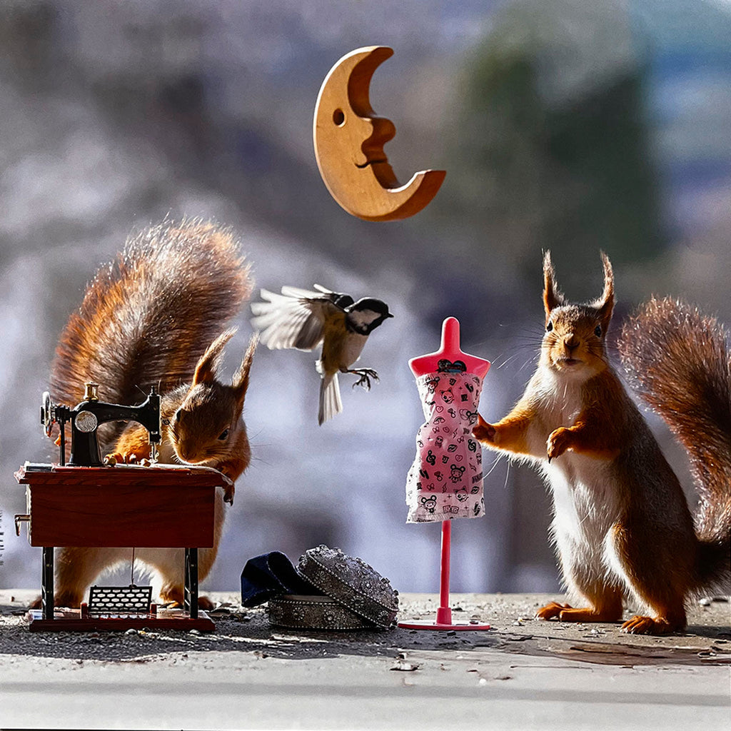 Two busy squirrels in a cute scene, one sewing a tiny dress on a miniature machine, the other holding a dress form, with a flying bird and wooden moon in the background – perfect for a funny animal calendar.