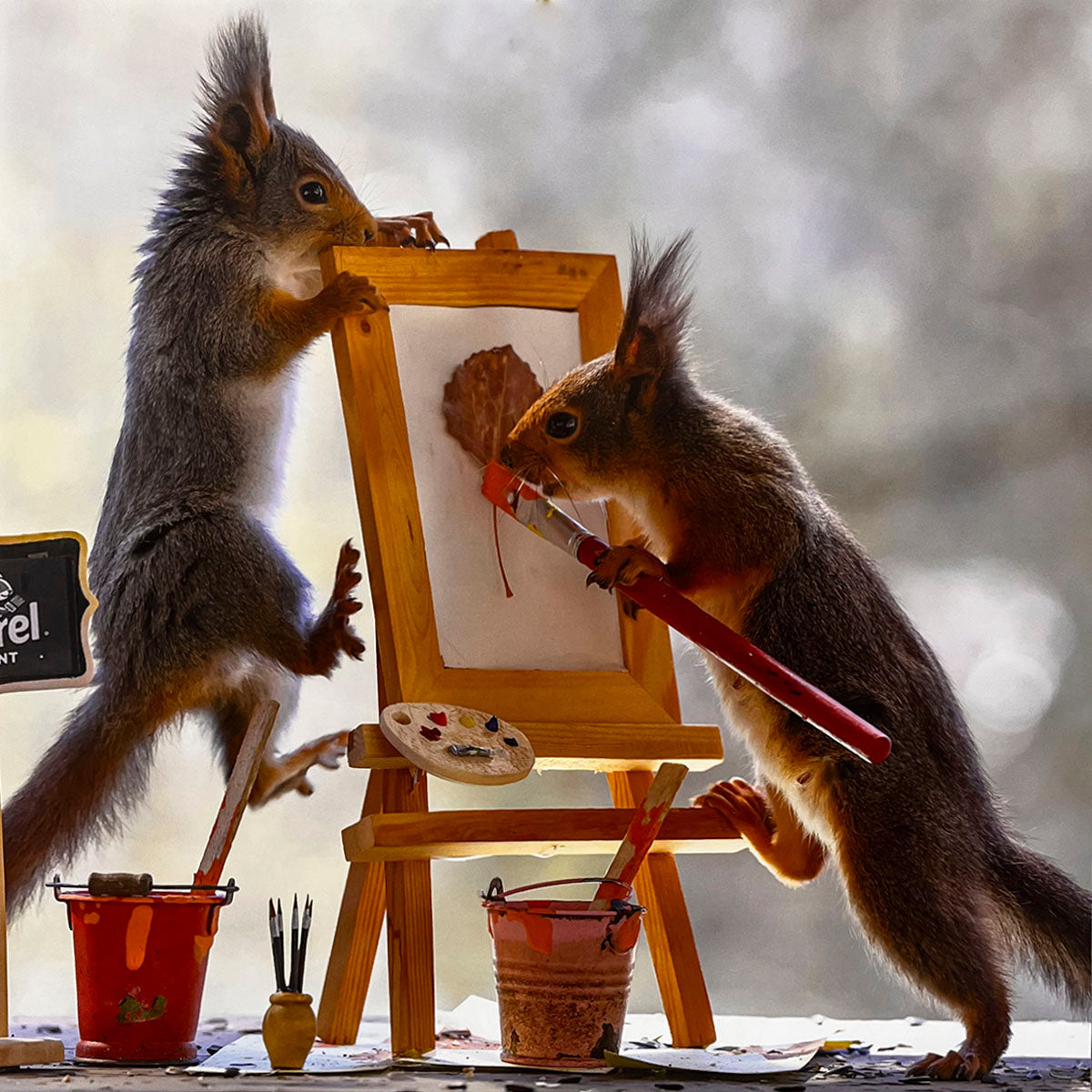 Two artistic squirrels working together on an easel, one painting with a brush and the other assisting, surrounded by paint buckets and palettes, an inspiring image for a creative calendar.