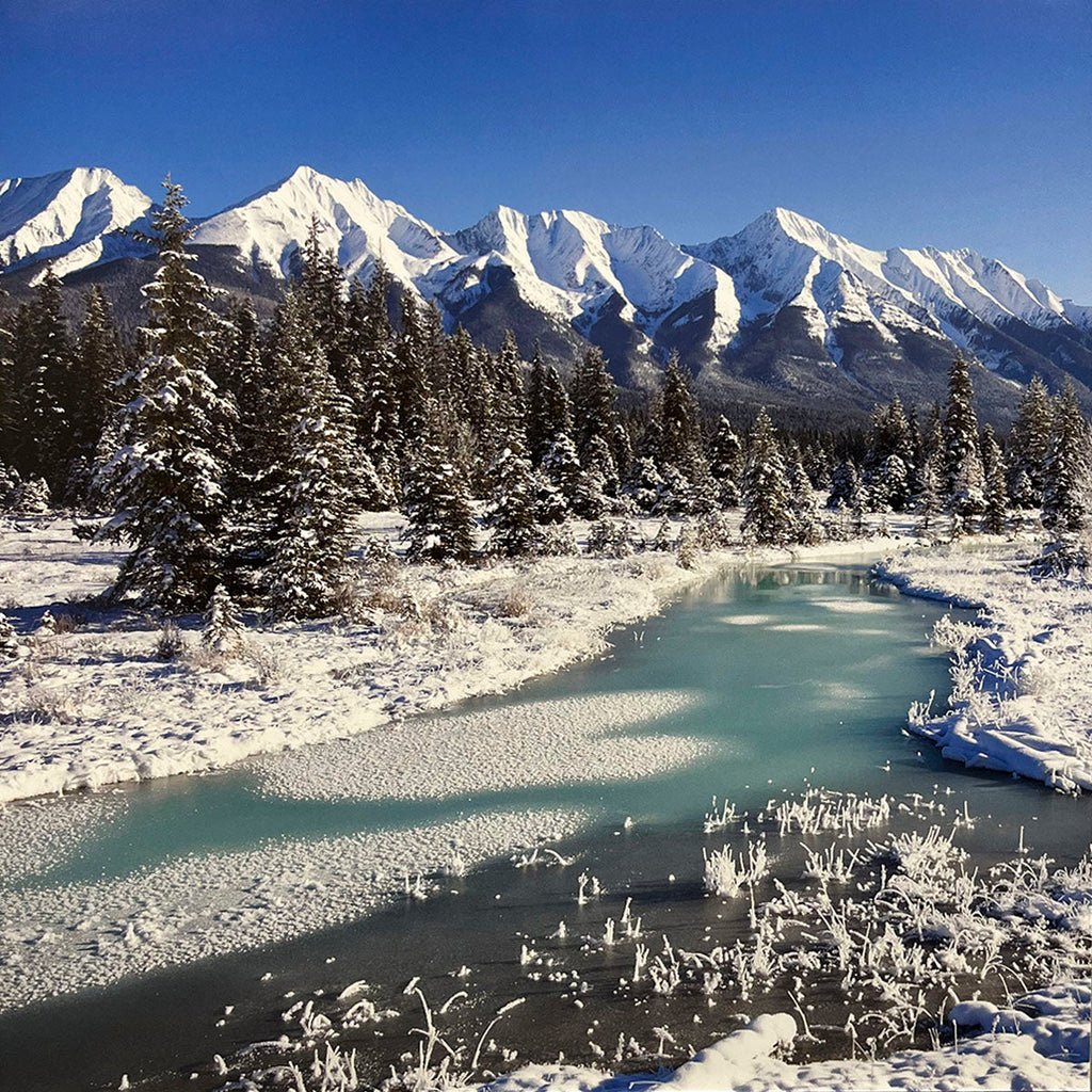 Winter mountain landscape for wall calendar featuring snow-capped peaks, a partially frozen turquoise river, and frosted pine trees under a clear blue sky. SEO: snowy mountains, winter calendar photo, frozen river, pine forest, nature scenery.