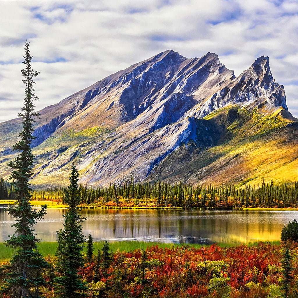 Autumn mountain landscape for wall calendar featuring a calm lake reflecting the vibrant yellow and orange trees lining its shores, with distant blue mountains under a cloudy sky. SEO: autumn lake, colorful trees, mountain landscape, calm water, fall calendar.