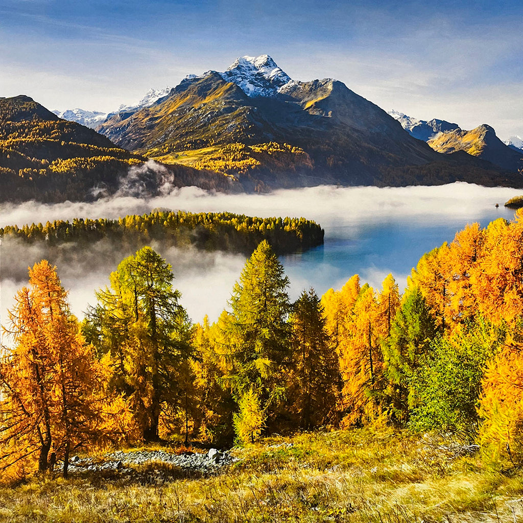 Foggy alpine lake scene for wall calendar, surrounded by brilliant yellow and orange autumn trees, with a snow-dusted mountain peak rising in the background under a blue sky. SEO: foggy lake, autumn trees, snow mountain, colorful landscape, scenic wall calendar.