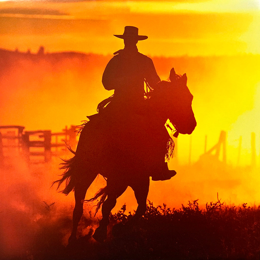 Dramatic silhouette of a cowboy riding a horse against a vibrant orange and yellow sunset, evoking the timeless spirit of the wild West.