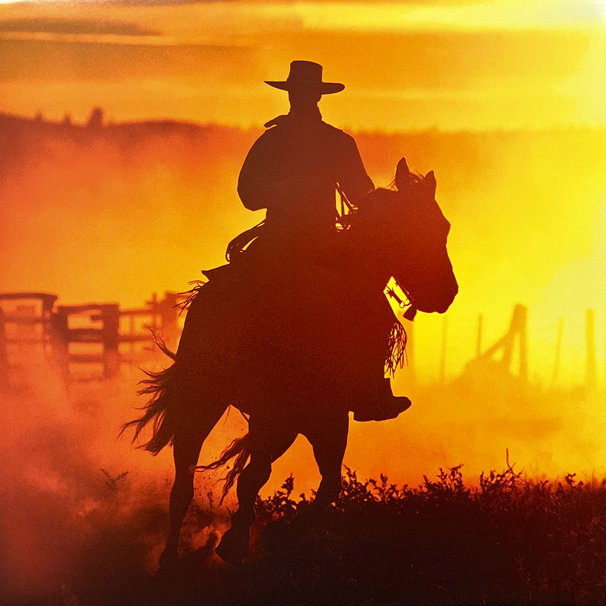 Dramatic silhouette of a cowboy riding a horse against a vibrant orange and yellow sunset, evoking the timeless spirit of the wild West.