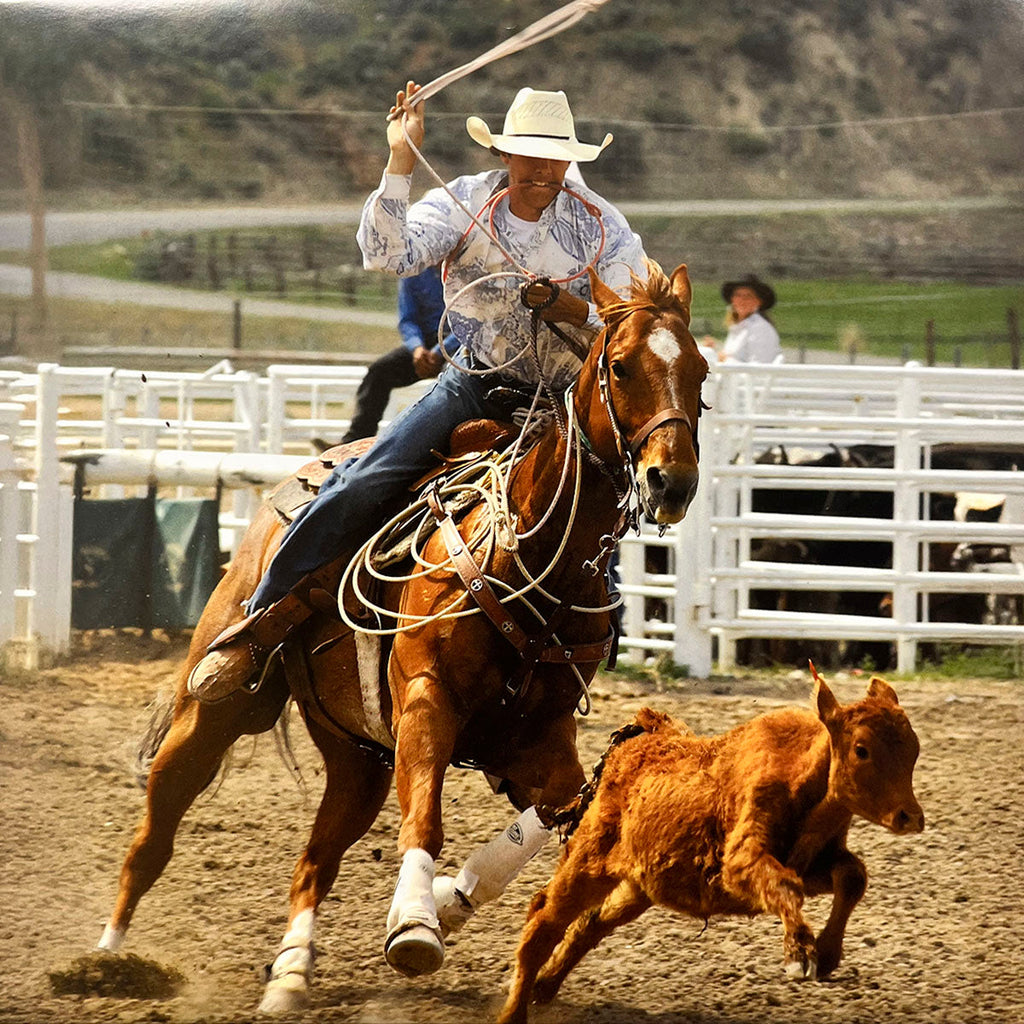 Action-packed image of a cowboy on a galloping horse expertly roping a calf in a dusty rodeo arena, highlighting Western sports.