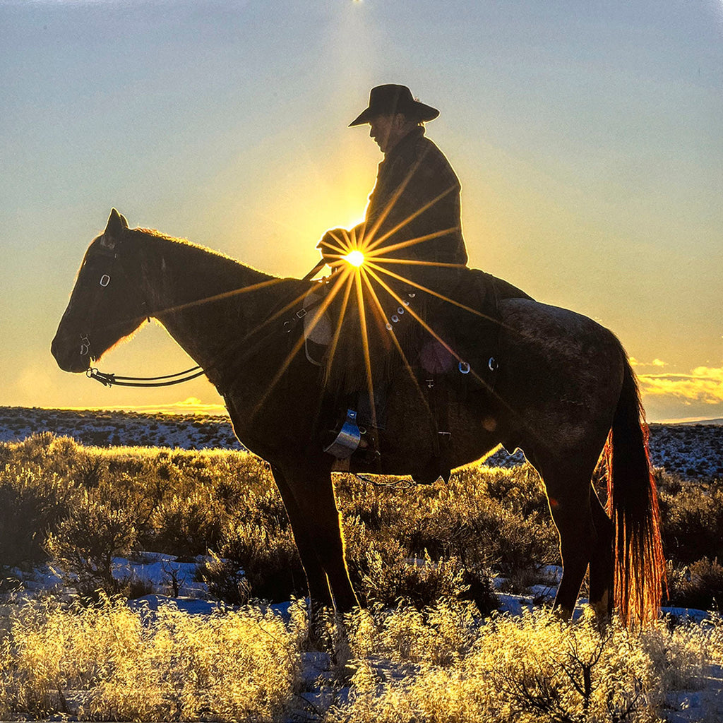 Serene silhouette of a cowboy on horseback against a brilliant sunrise over a snowy, sparse Western landscape, radiating peace and hope.