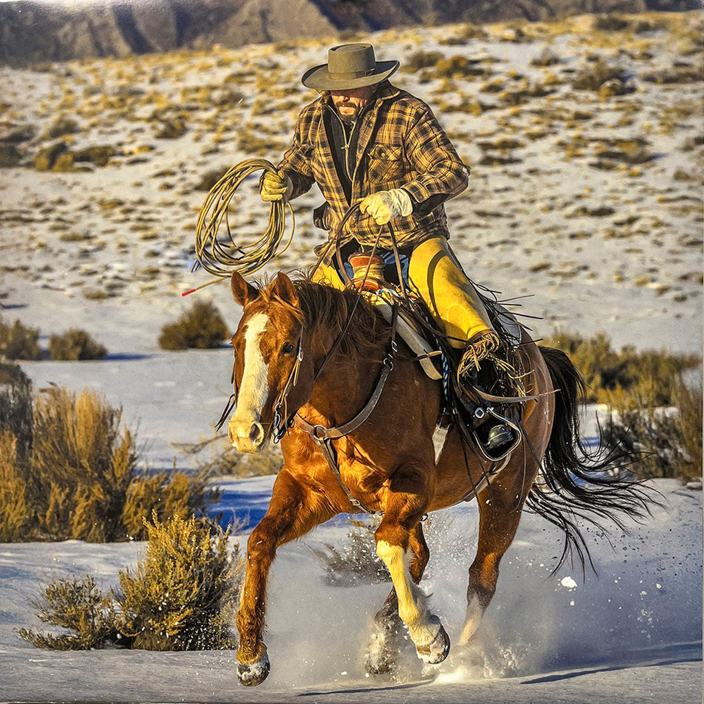 Dynamic scene of a cowboy on a brown and white horse galloping through light snow, holding a rope, wearing a plaid shirt and hat, for a Western calendar.