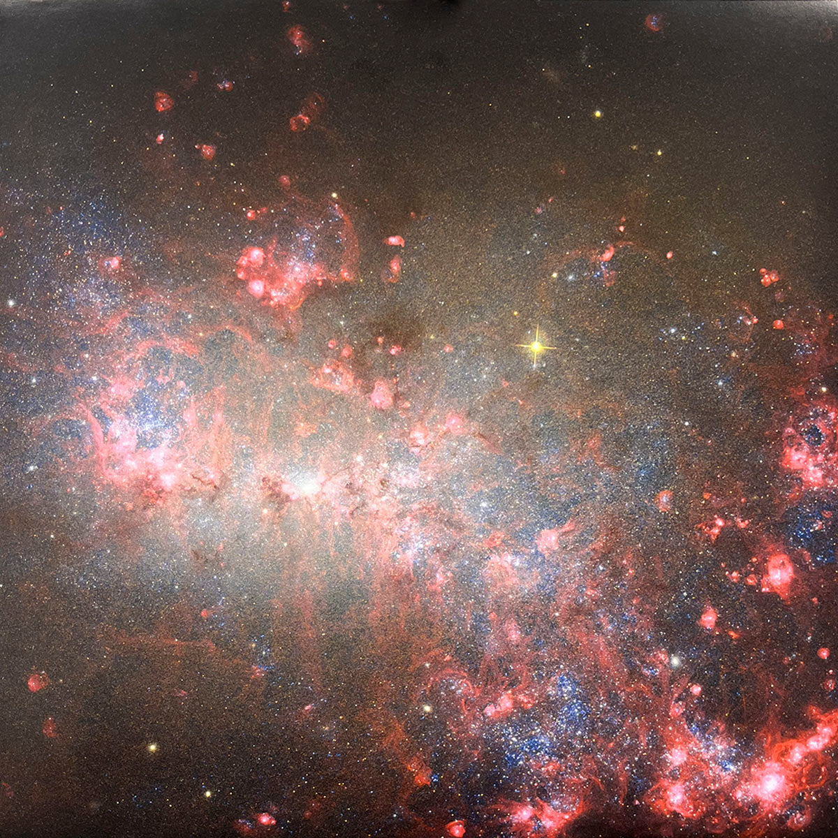 Irregular galaxy exhibiting diffuse, glowing red gas clouds and bright, energetic blue star clusters scattered throughout.