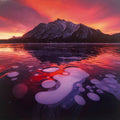 Breathtaking sunset over Abraham Lake, Alberta, Canada, with vibrant red and orange sky reflecting on a frozen lake with unique methane ice bubbles and a majestic mountain backdrop. SEO optimized for nature calendar, scenic photography, wall art.